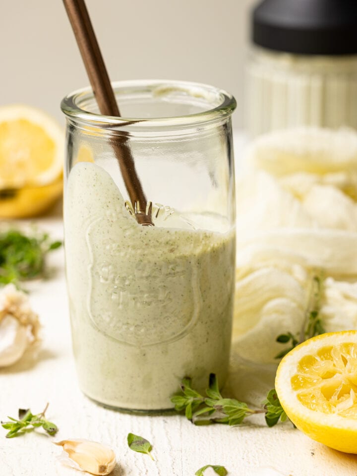 Lemon garlic dressing in a mason jar with a spoon on a white table.