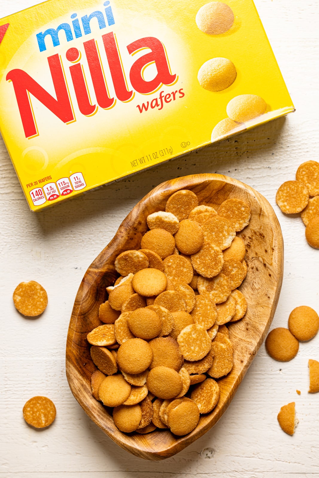 Nilla wafer cookies in the box and in a wooden bowl on a white table.