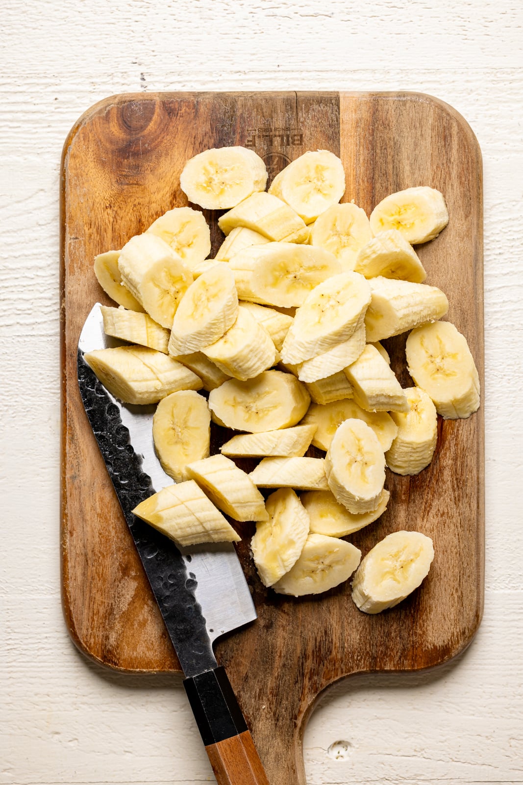 Bananas sliced on a cutting board with a knife on a white table.