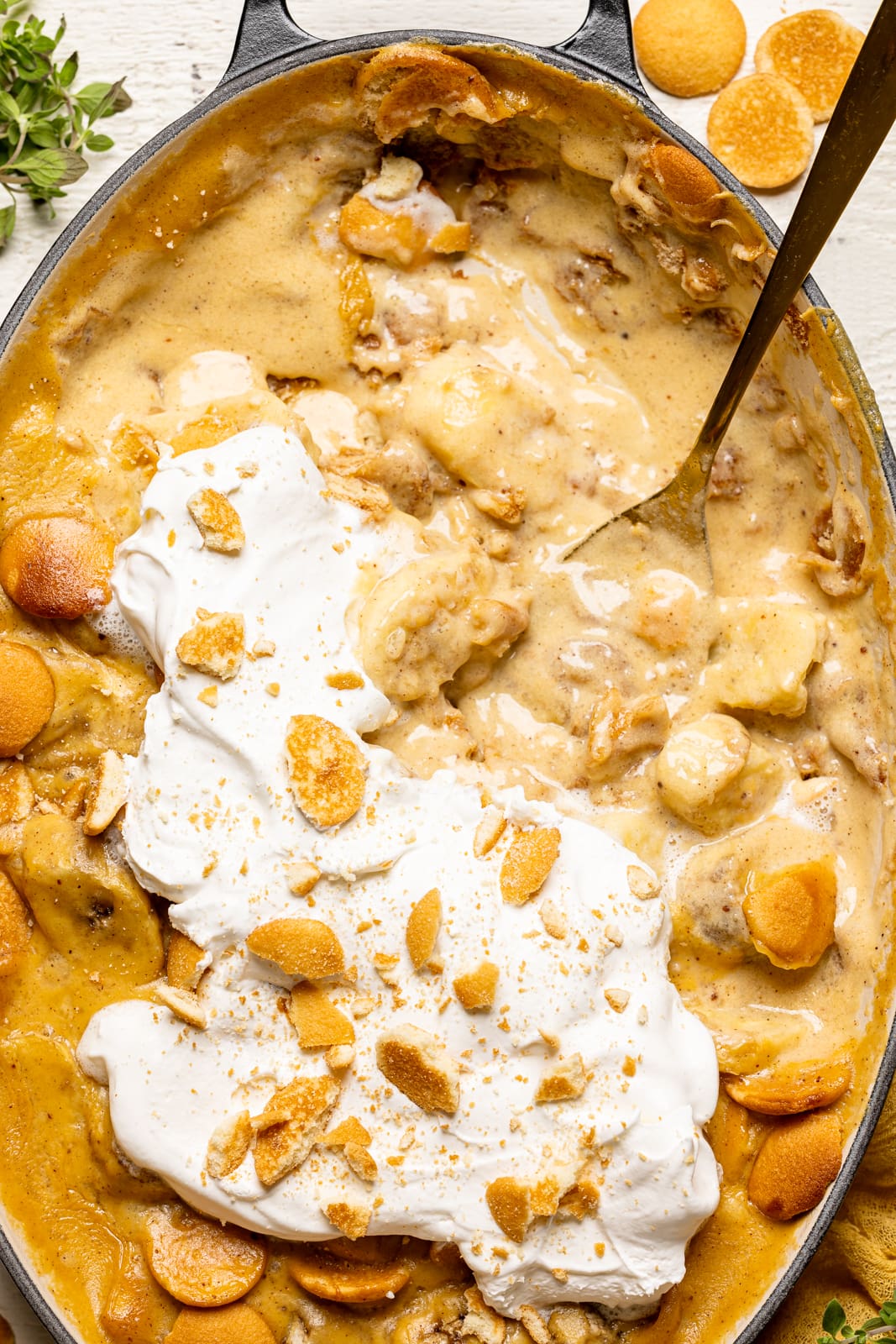 Baked banana pudding in a baking dish half scooped out with a spoon on a white table.