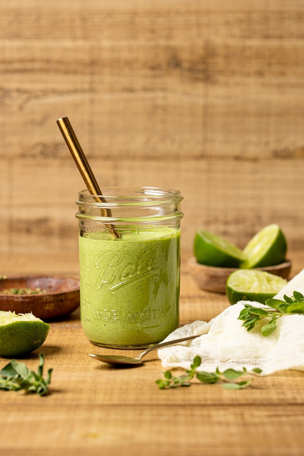 Green goddess dressing in a mason jar with a spoon on a brown wood table with limes.