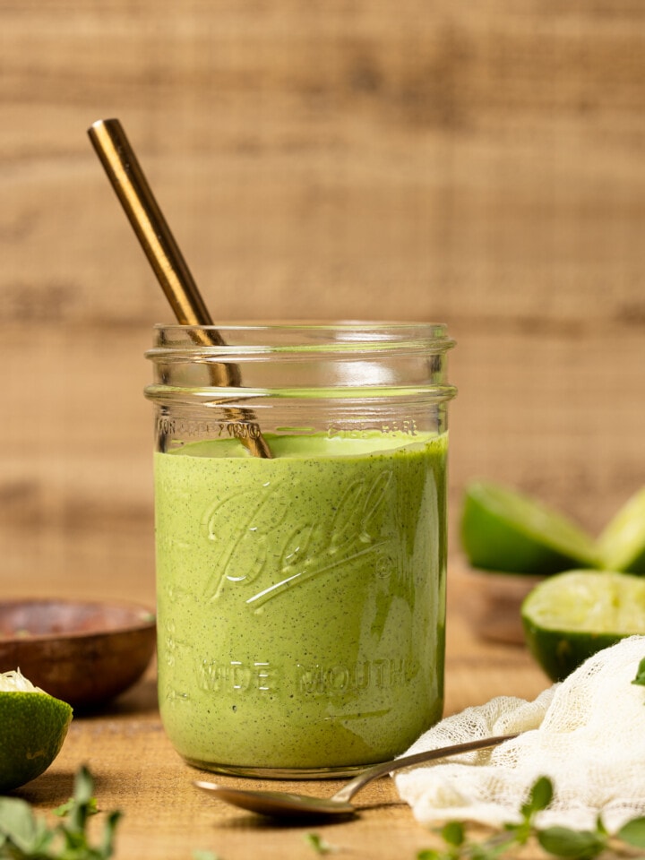 Green goddess dressing in a mason jar with a spoon on a brown wood table with limes.