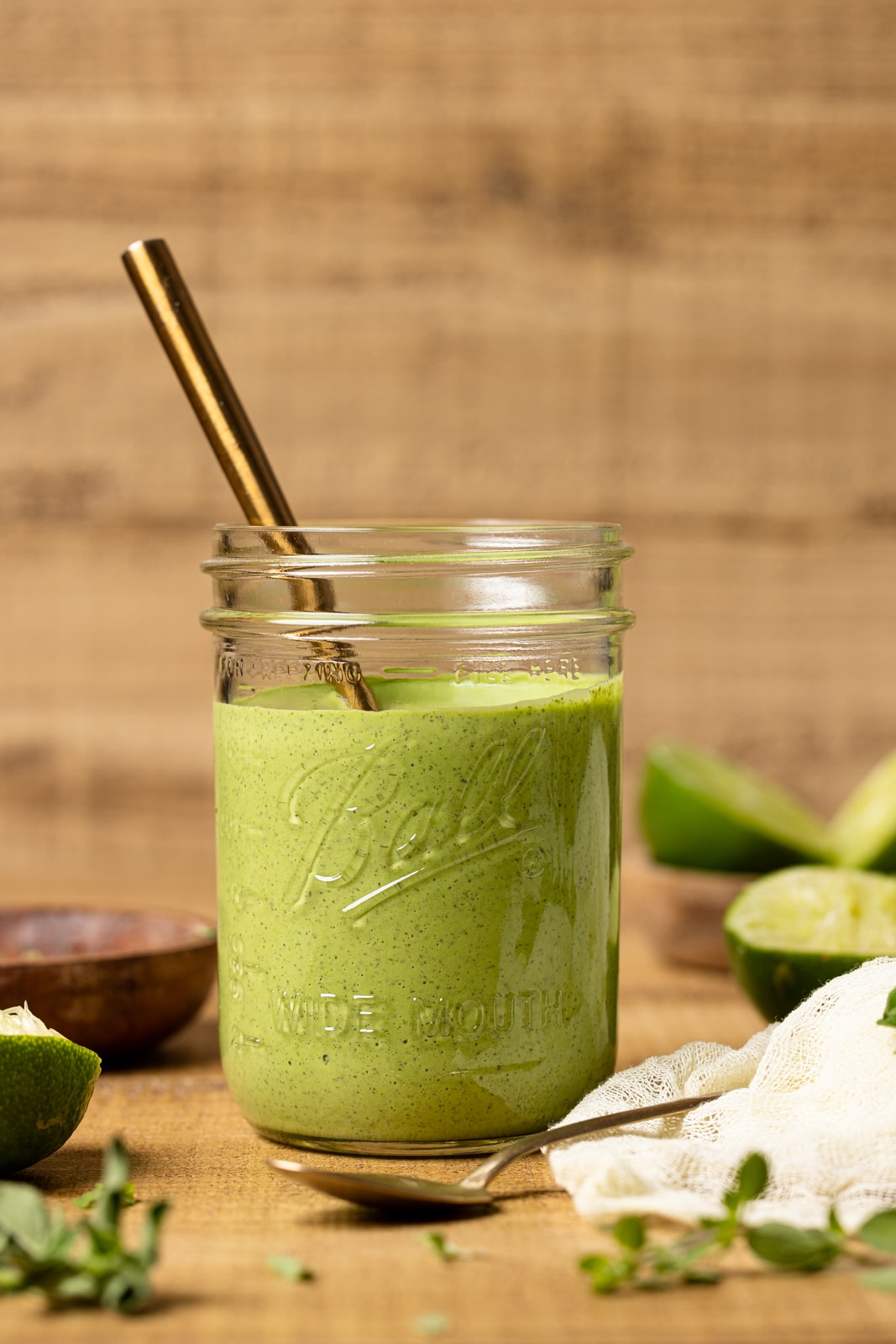 Green goddess dressing in a mason jar with a spoon on a brown wood table with limes.