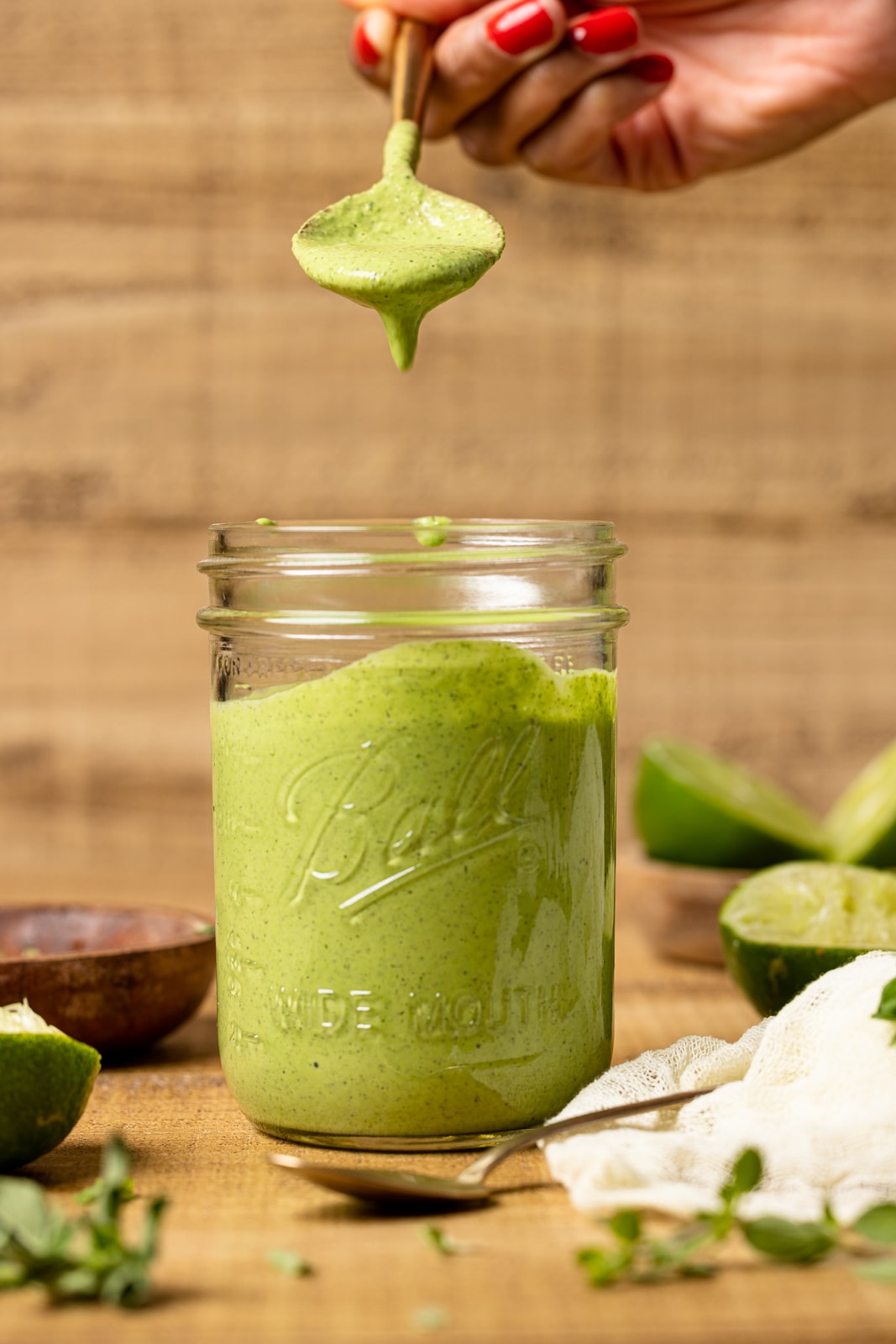 Spoon dripping with green goddess dressing from a mason jar on a brown wood table.