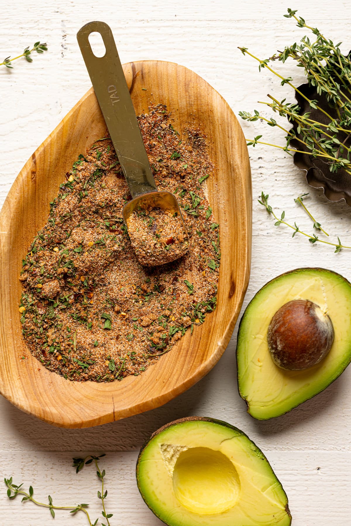 Wooden bowl of spices next to an opened avocado