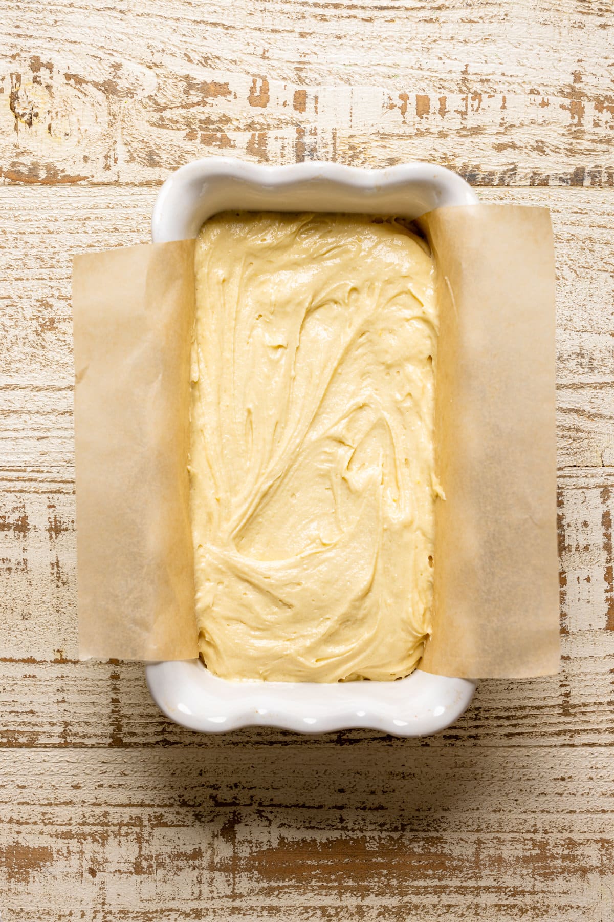 Loaf pan lined with parchment paper and filled with lemon pound cake batter