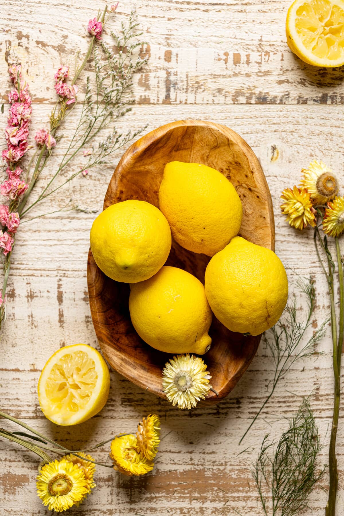 Wooden bowl of lemons surrounded by flowers