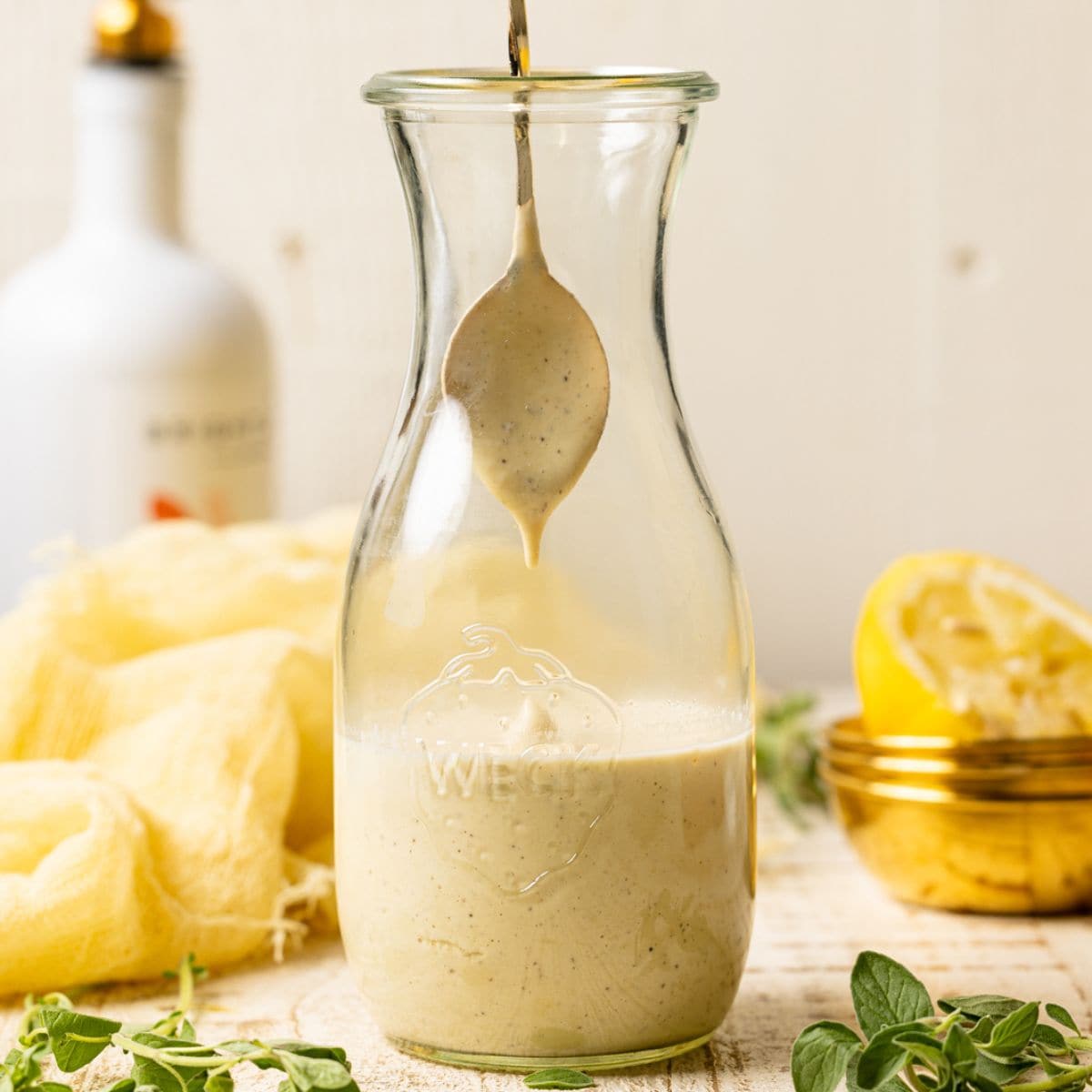Honey mustard dressing in a jar with a spoon being help up with a bit of dressing on it on a white table.