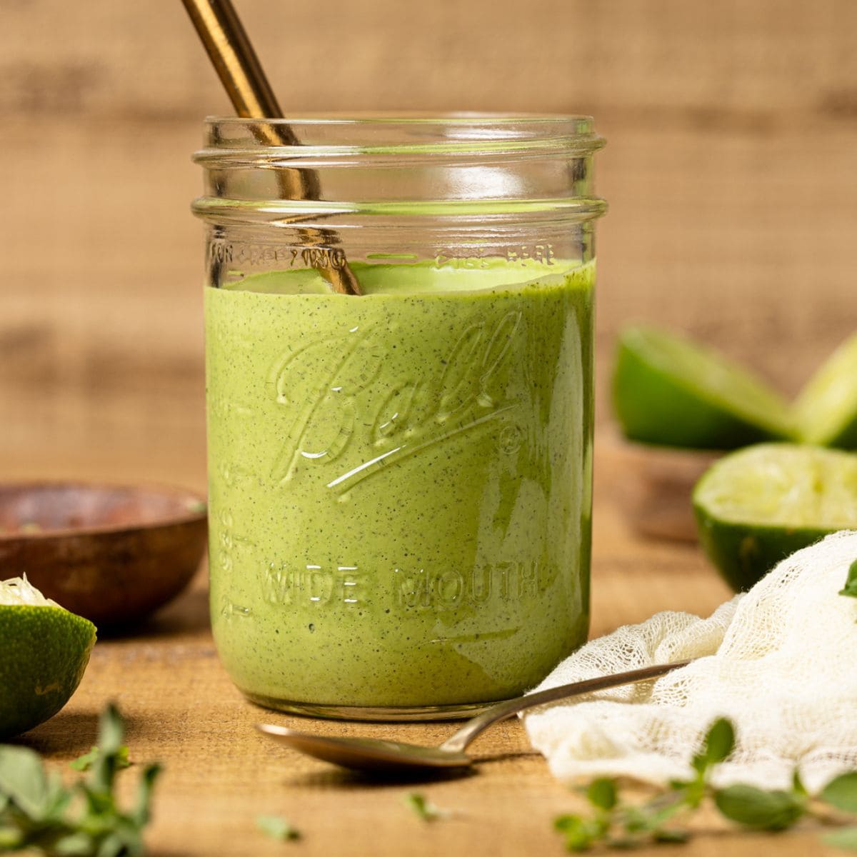 Green goddess dressing in a mason jar with a spoon on a brown wood table with limes.