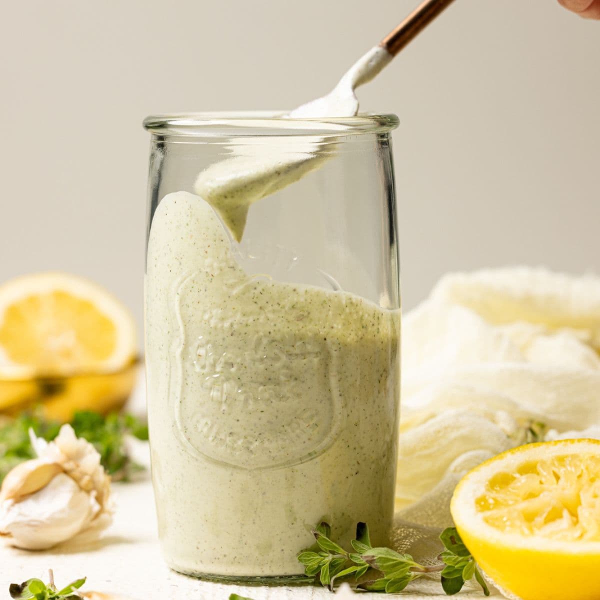 Lemon garlic dressing in a mason jar being scooped up with a spoon on a white table.