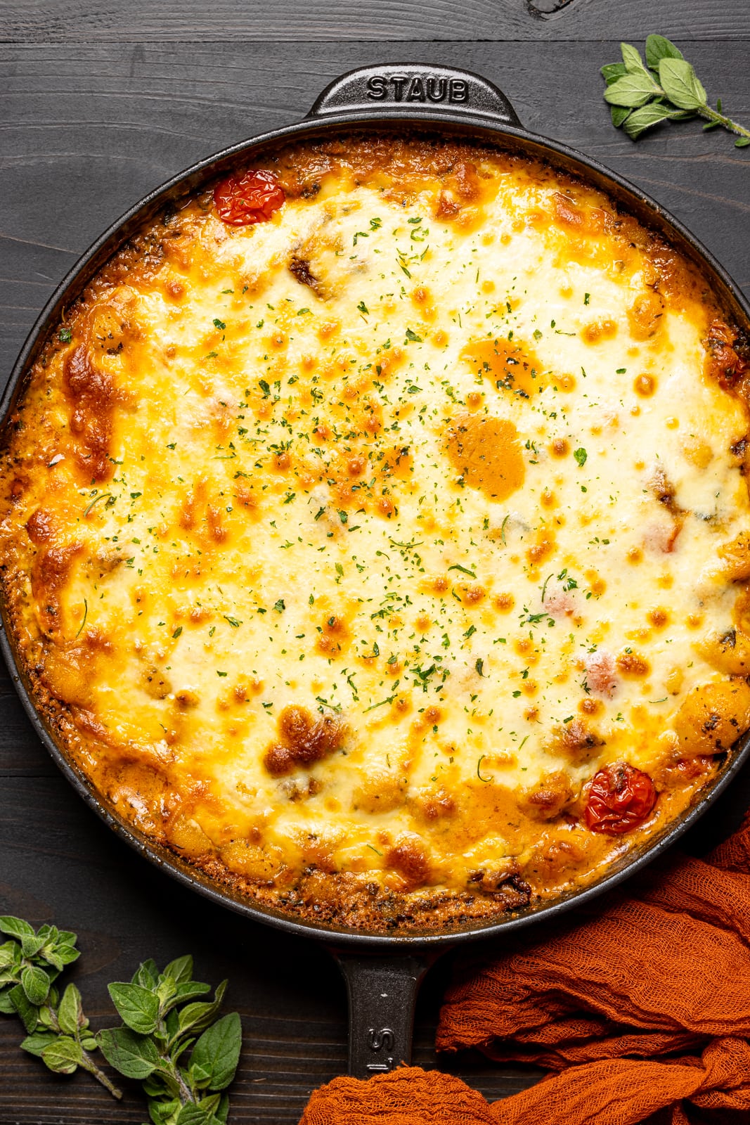 Baked chicken and gnocchi in a skillet on a black table.