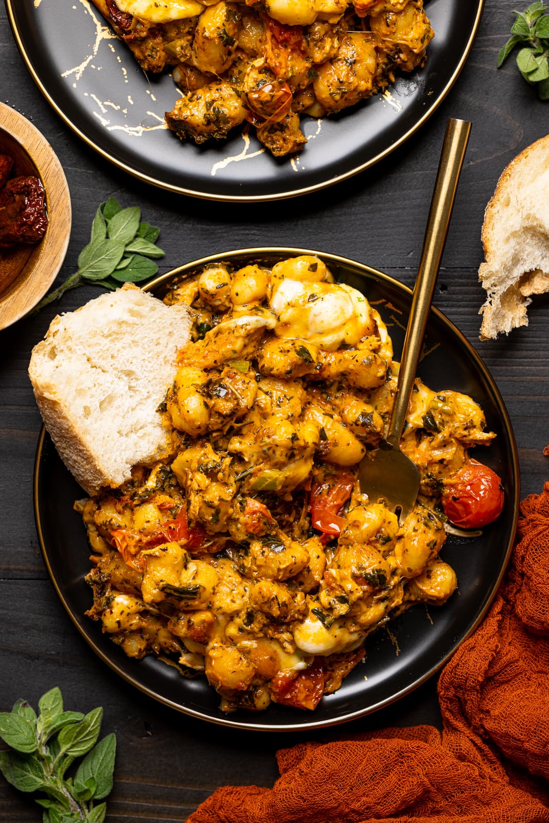 Baked chicken and gnocchi on a black plate with a side of bread and a fork on a black table.