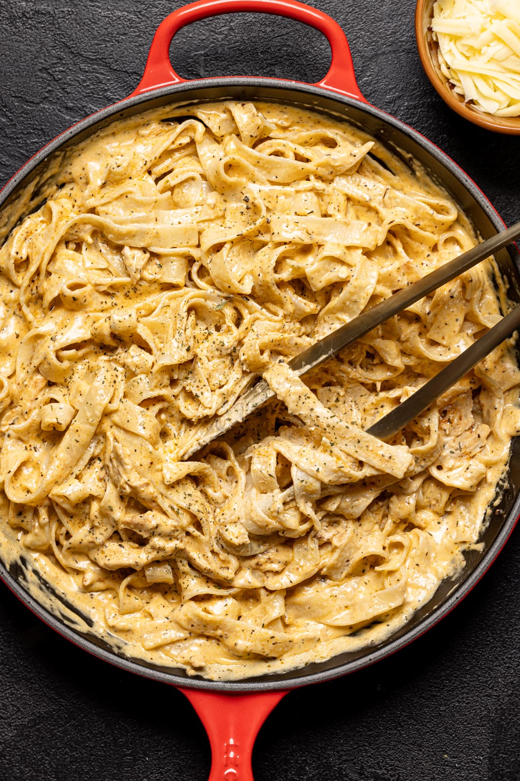 Creamy alfredo in a large red skillet with tongs.