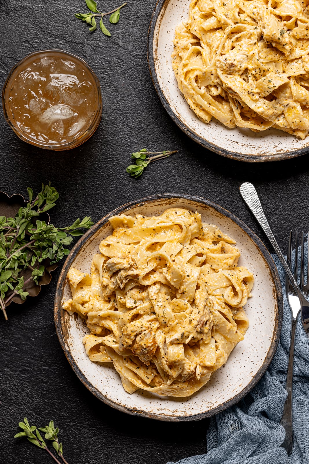 Alfredo on two white plates with two forks and a drink on a black table.