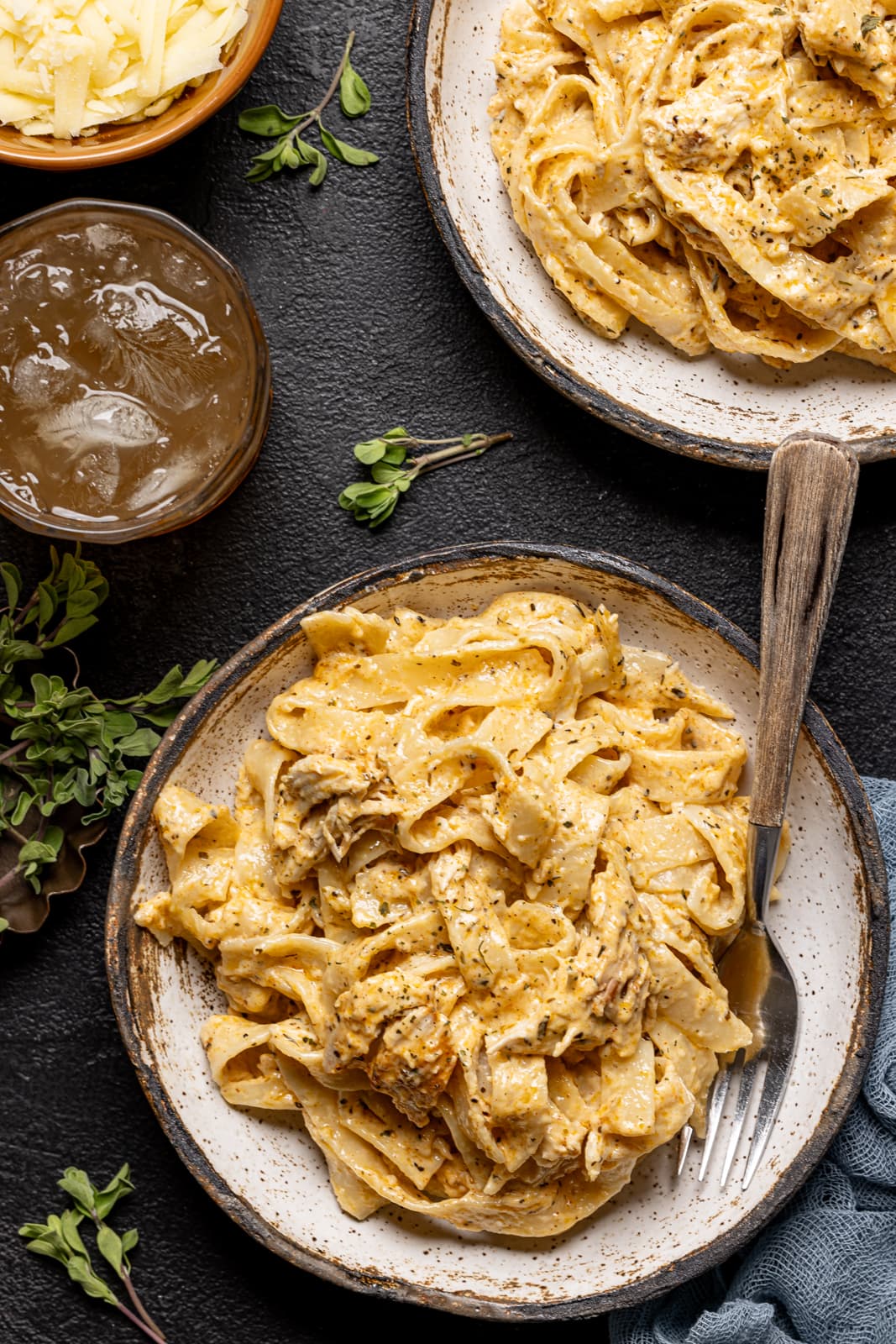 Alfredo on two white plates with two forks and a drink on a black table.