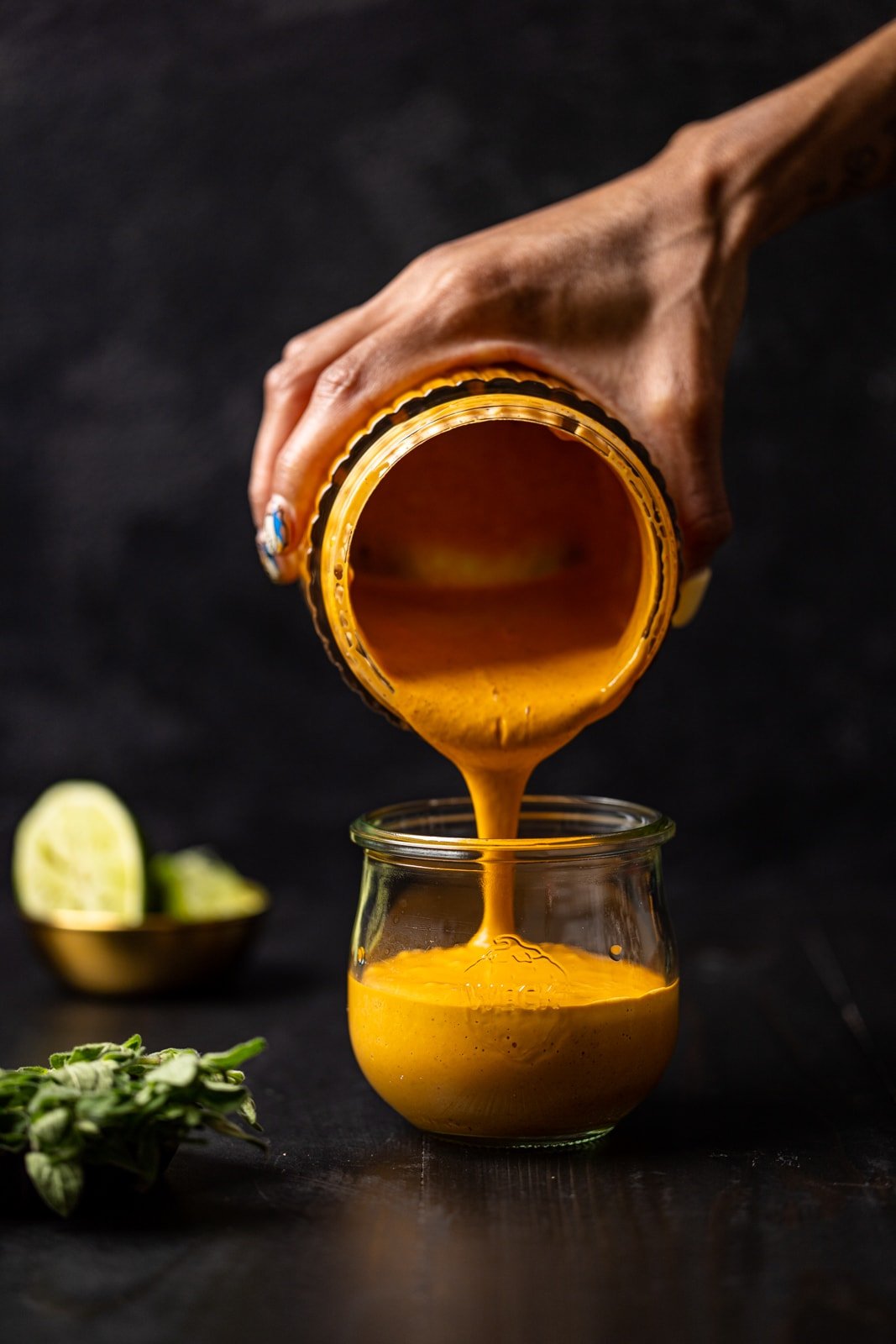 Chipotle sauce being poured from blender to a mason jar on a black table with lime wedges.