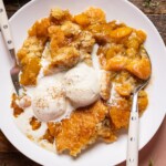 Up close shot of peach cobbler in a low bowl with scoops of ice cream.