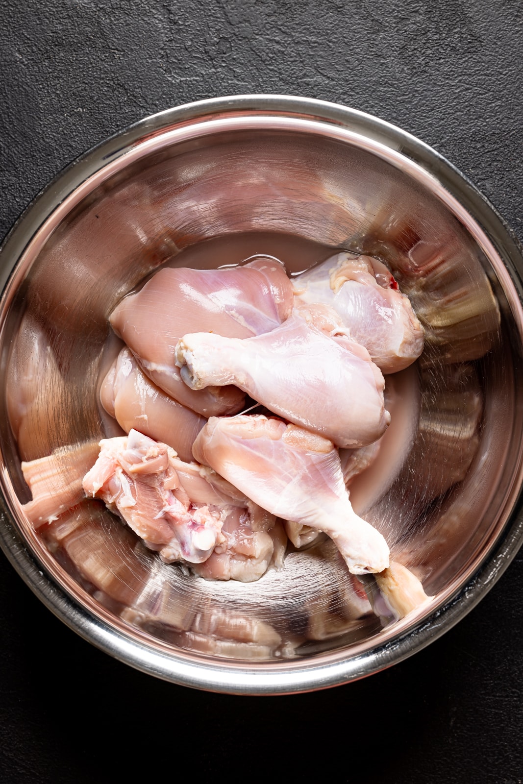 Uncooked chicken in a large silver bowl on a black table.