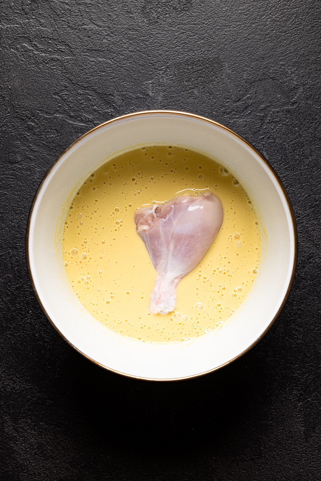 Chicken in wet batter in a white bowl on a black table.