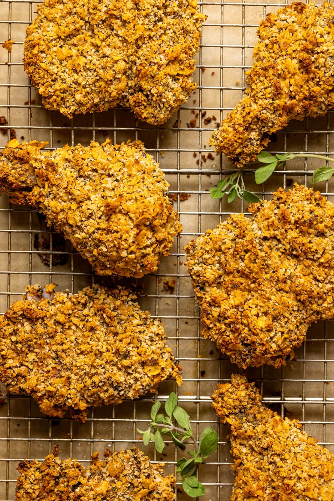 Baked fried chicken on a baking sheet with a wire rack and herbs as garnish.