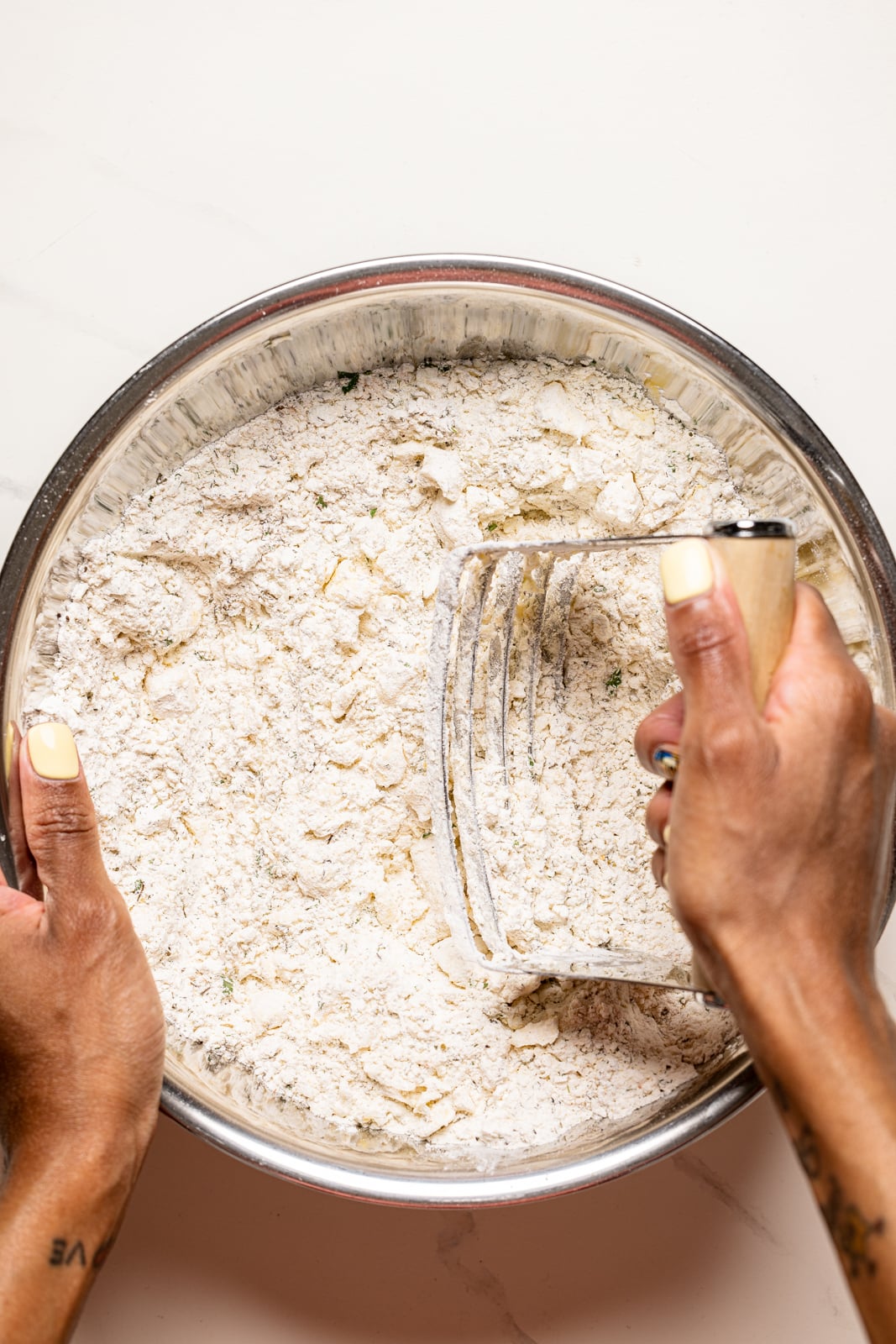 Dry ingredients in a large silver bowl on a marble table being mixed.