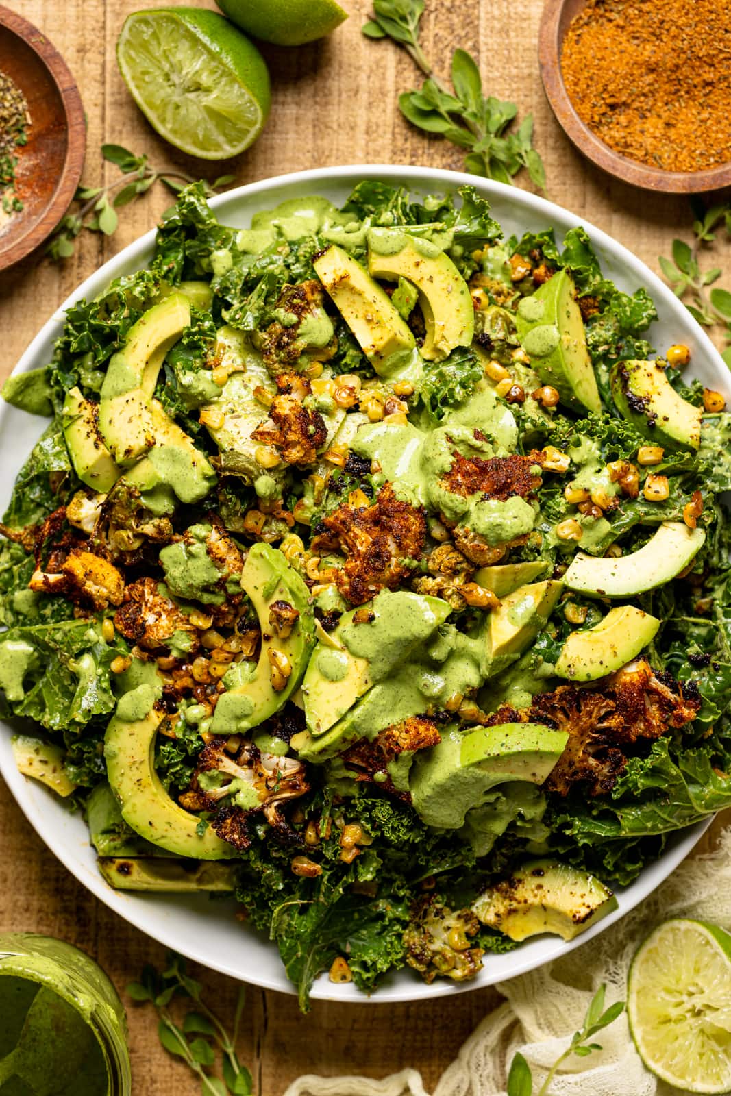 Salad on a white round plate with seasonings and herbs, lime wedges, dressing, and a yellow napkin.