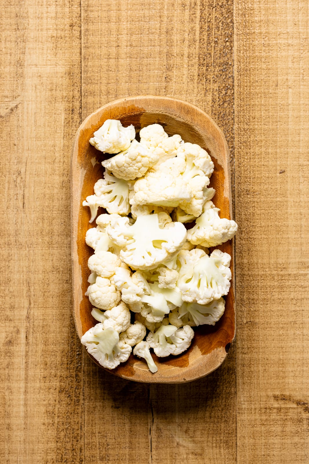 Cauliflower florets in a brown bowl on a wood table.