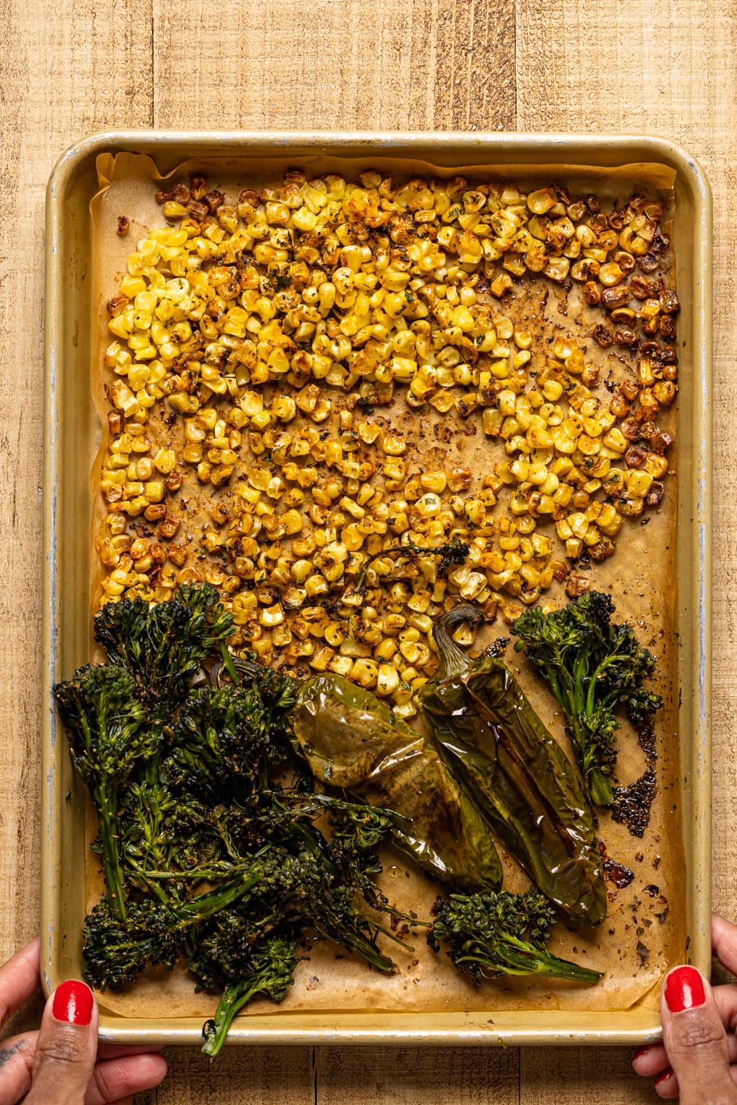 Roasted broccolini and corn on a sheet pan on a wood table.