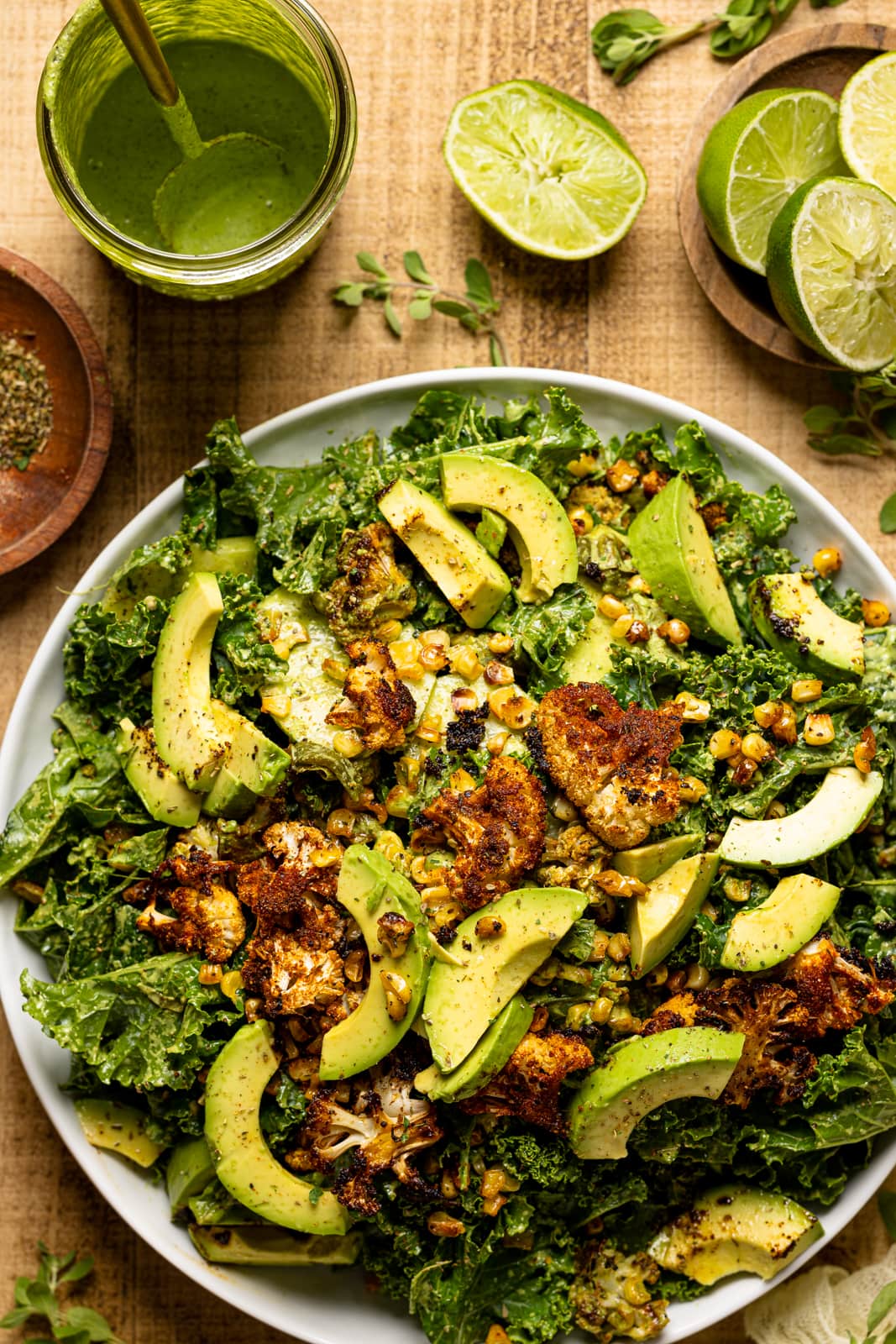 Salad on a round white plate with lime wedges and dressing on a wood table.