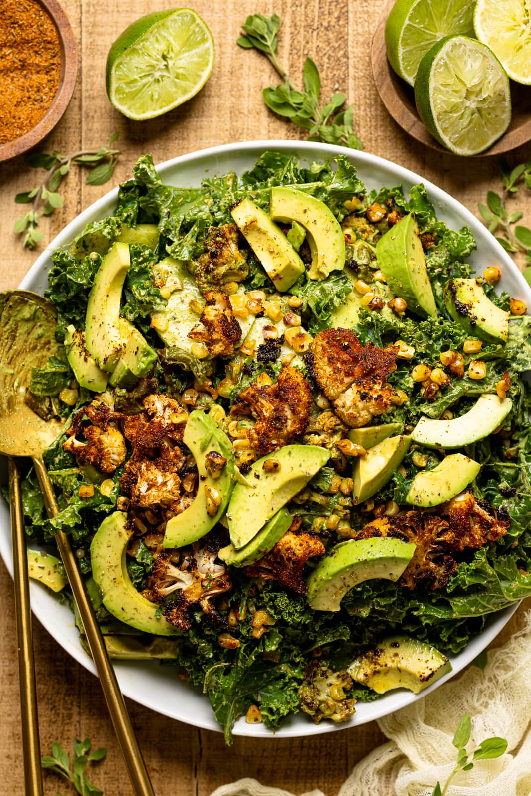 Salad on a white round plate with two gold serving spoons and lime wedges.