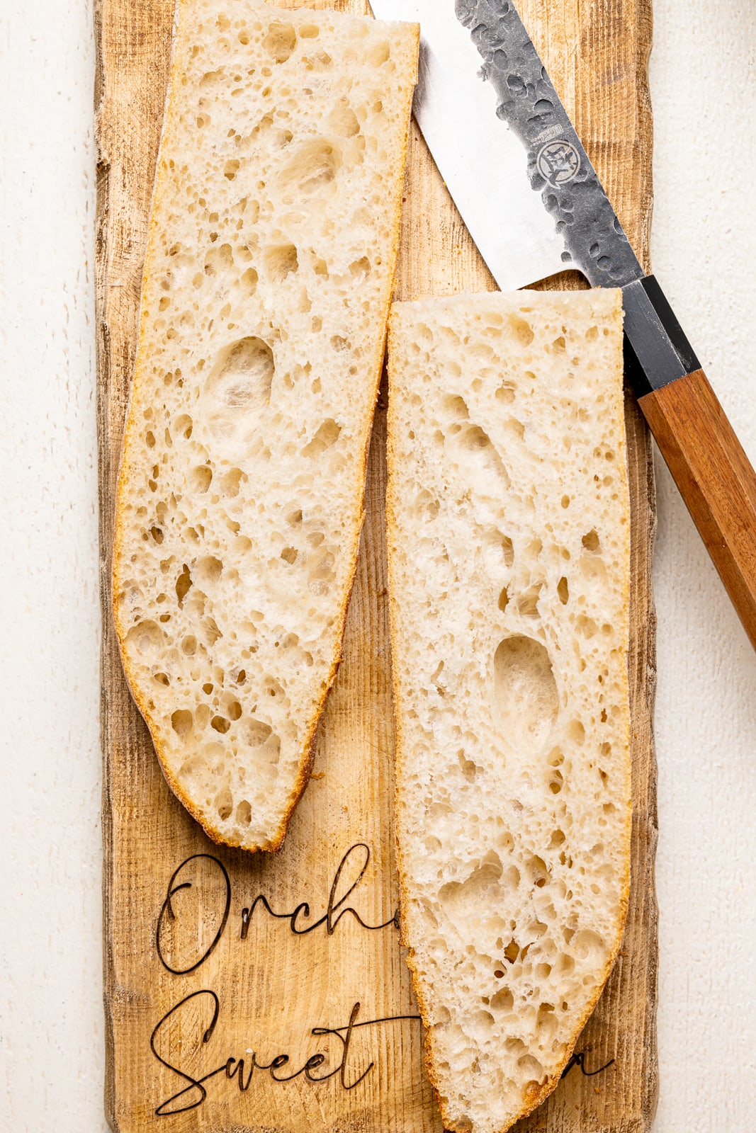 Two slices of french bread on a cutting board with a knife on a white wood table.