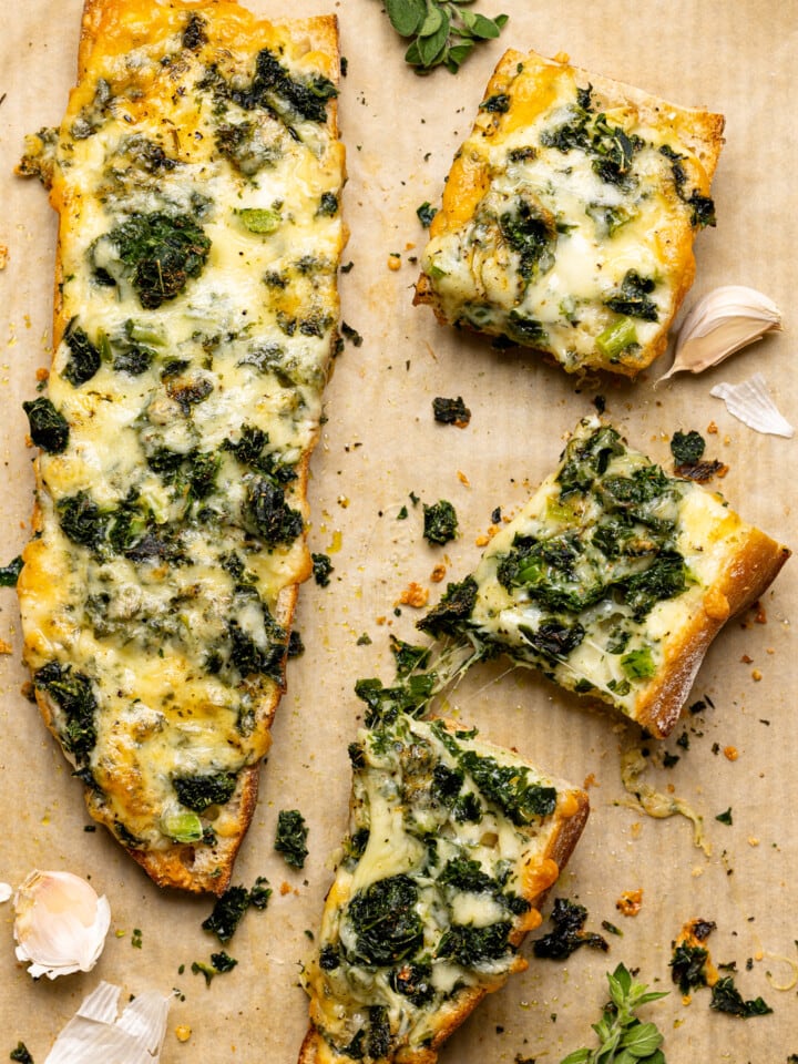 Baked french bread sliced on a baking sheet on a parchment paper with garlic and herbs.