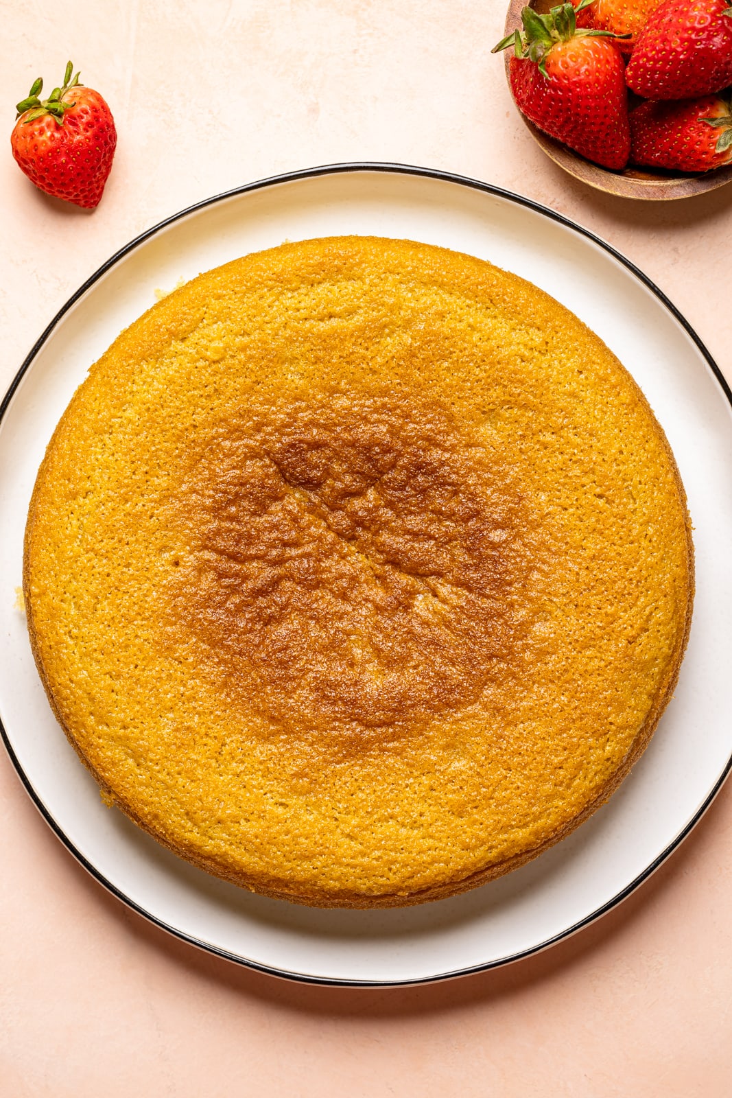 Baked cake on a white plate with strawberries on a peach colored table.