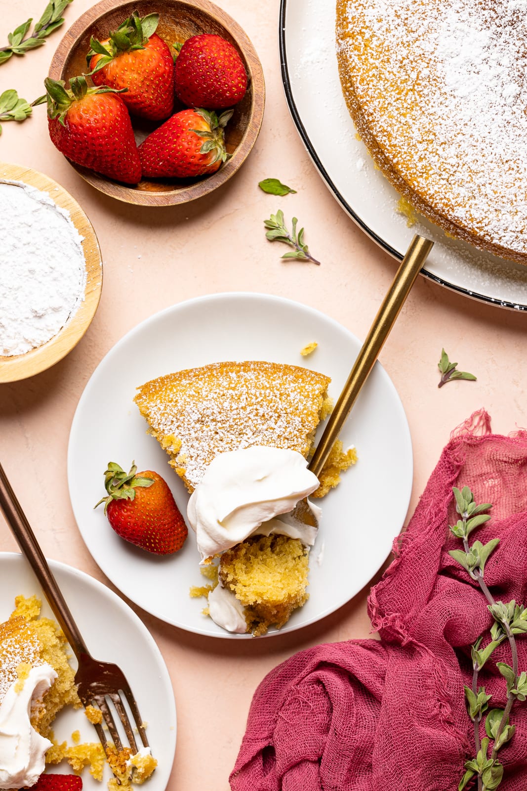 Cake slices on white plates with fork, whipped cream, and strawberries on a peach colored table. 