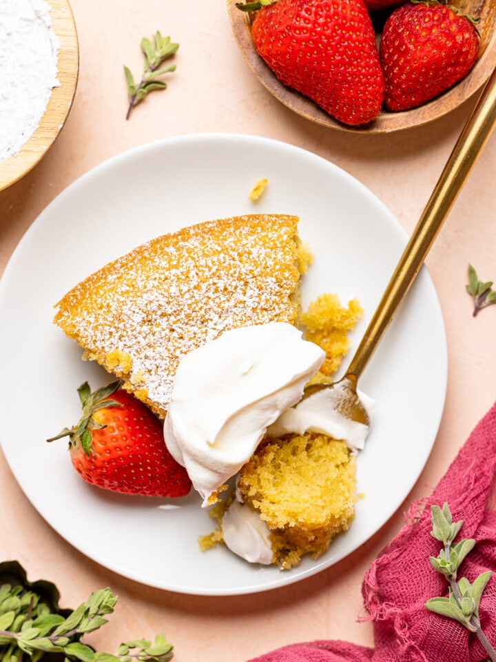 Up close shot of slice of cake on a white plate with whipped cream, strawberries, and fork on a peach colored table.