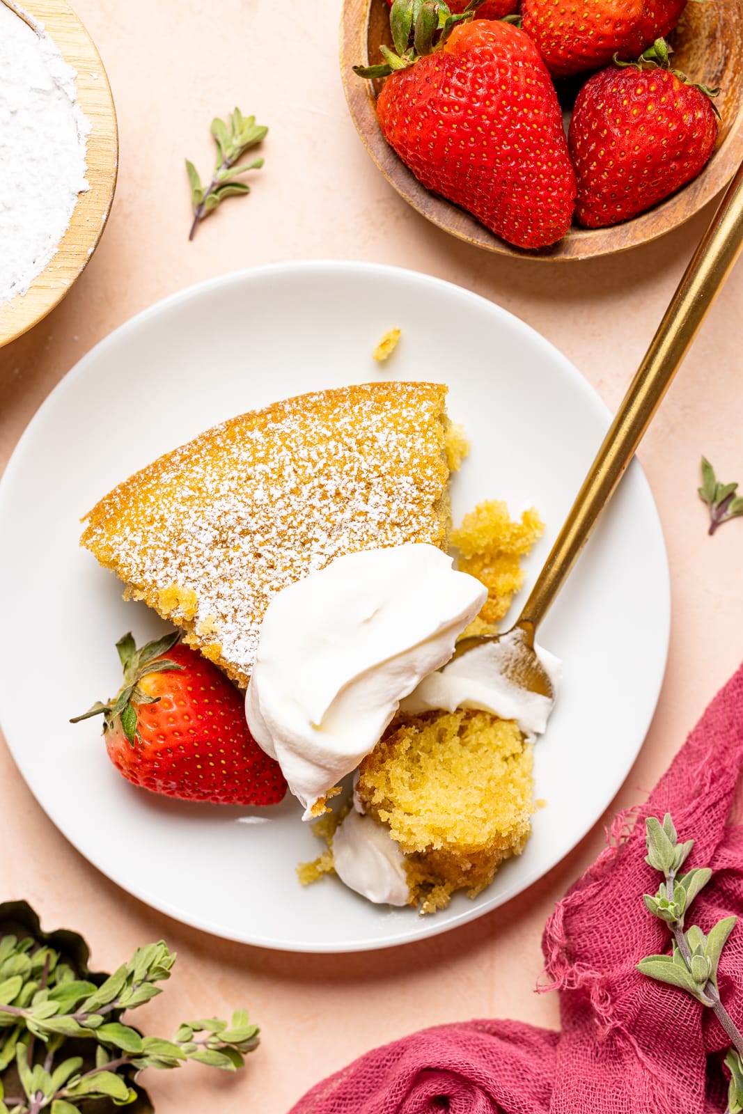 Up close shot of slice of cake on a white plate with whipped cream, strawberries, and fork on a peach colored table.