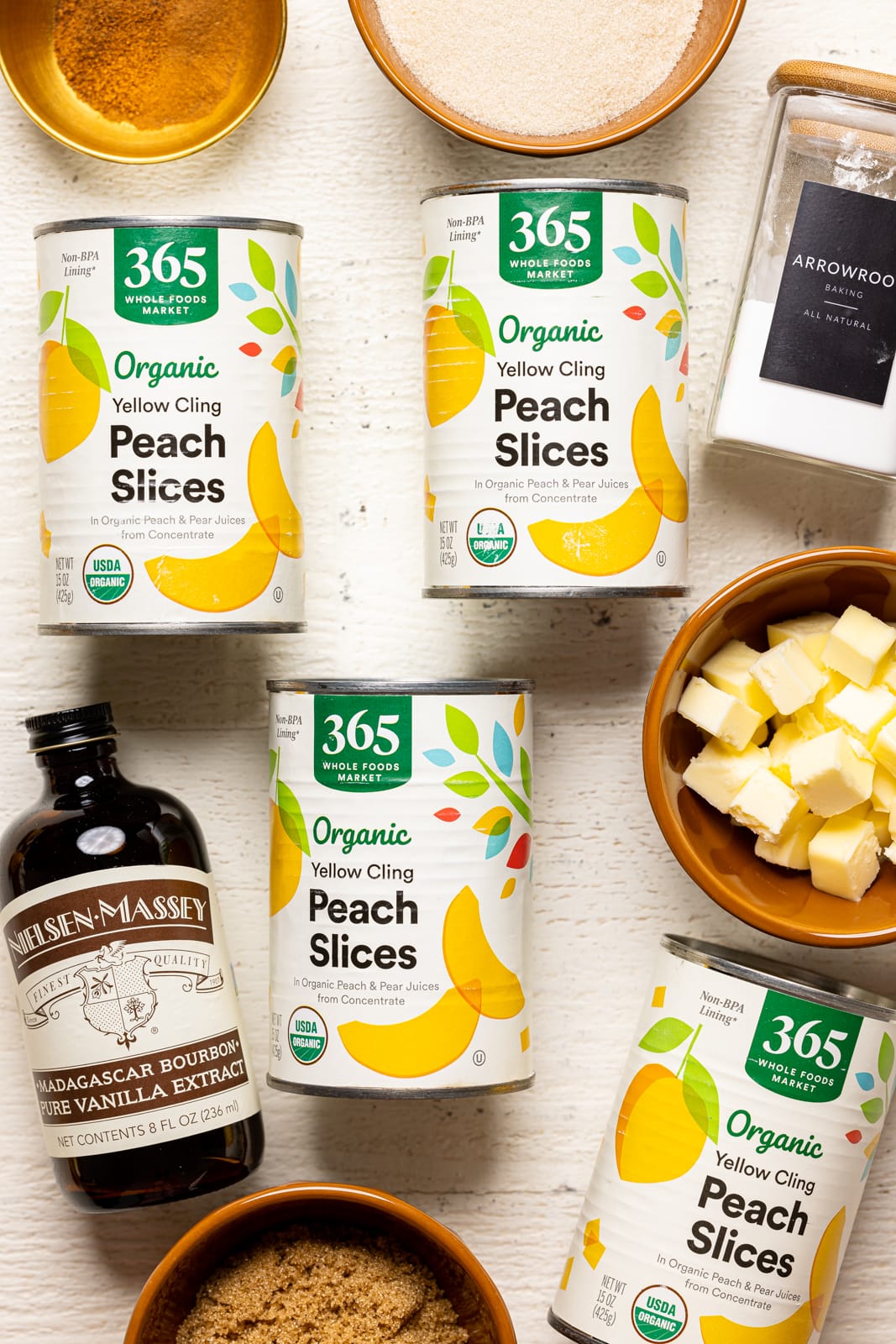 Ingredients on a white wood table including canned peaches, vanilla, brown sugar, arrowroot, and sugar.