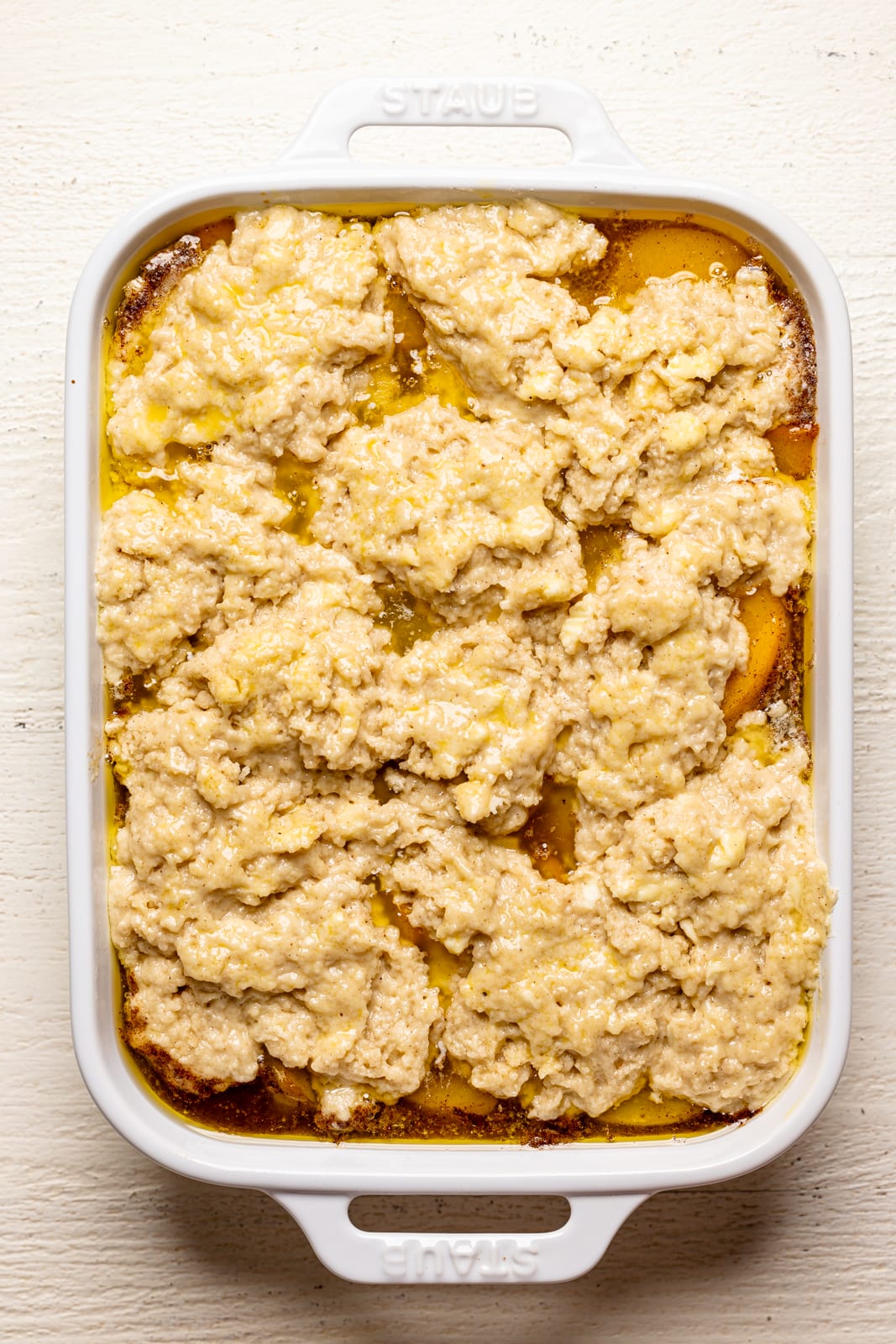 Peach cobbler in a white baking dish on a white wood table.
