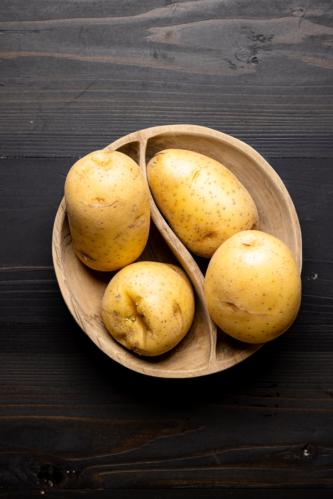Potatoes in a wood bowl on a black table.