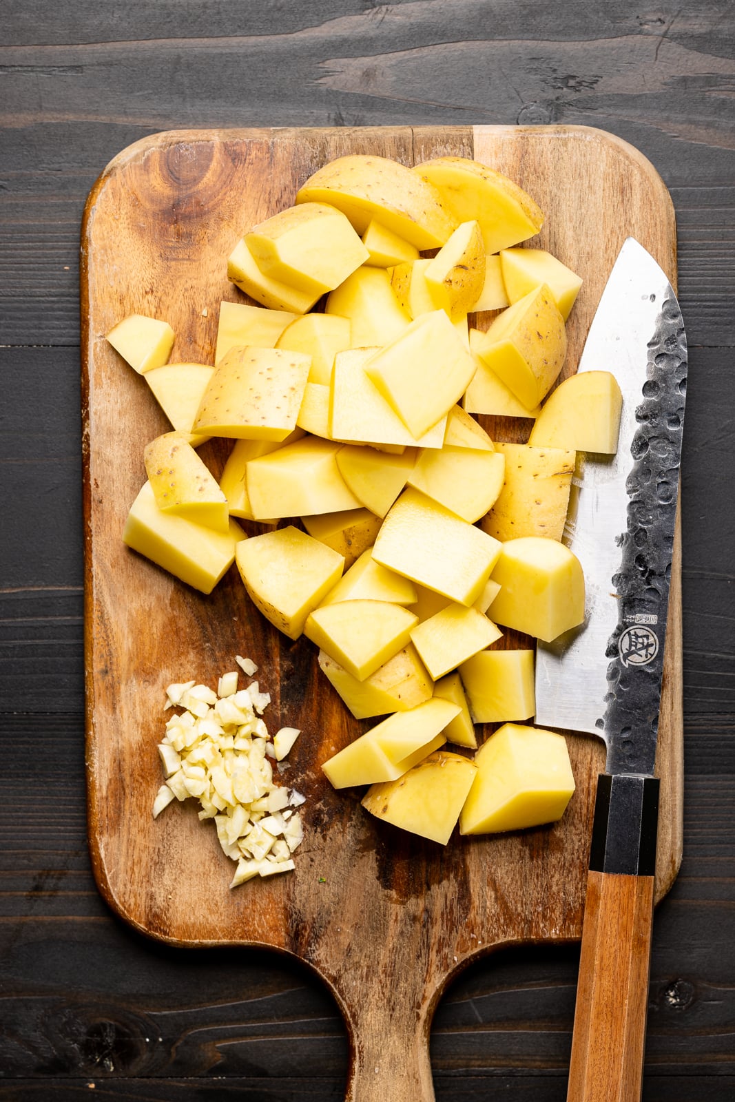 Chopped potatoes on a brown cutting board with a knife on a black table.