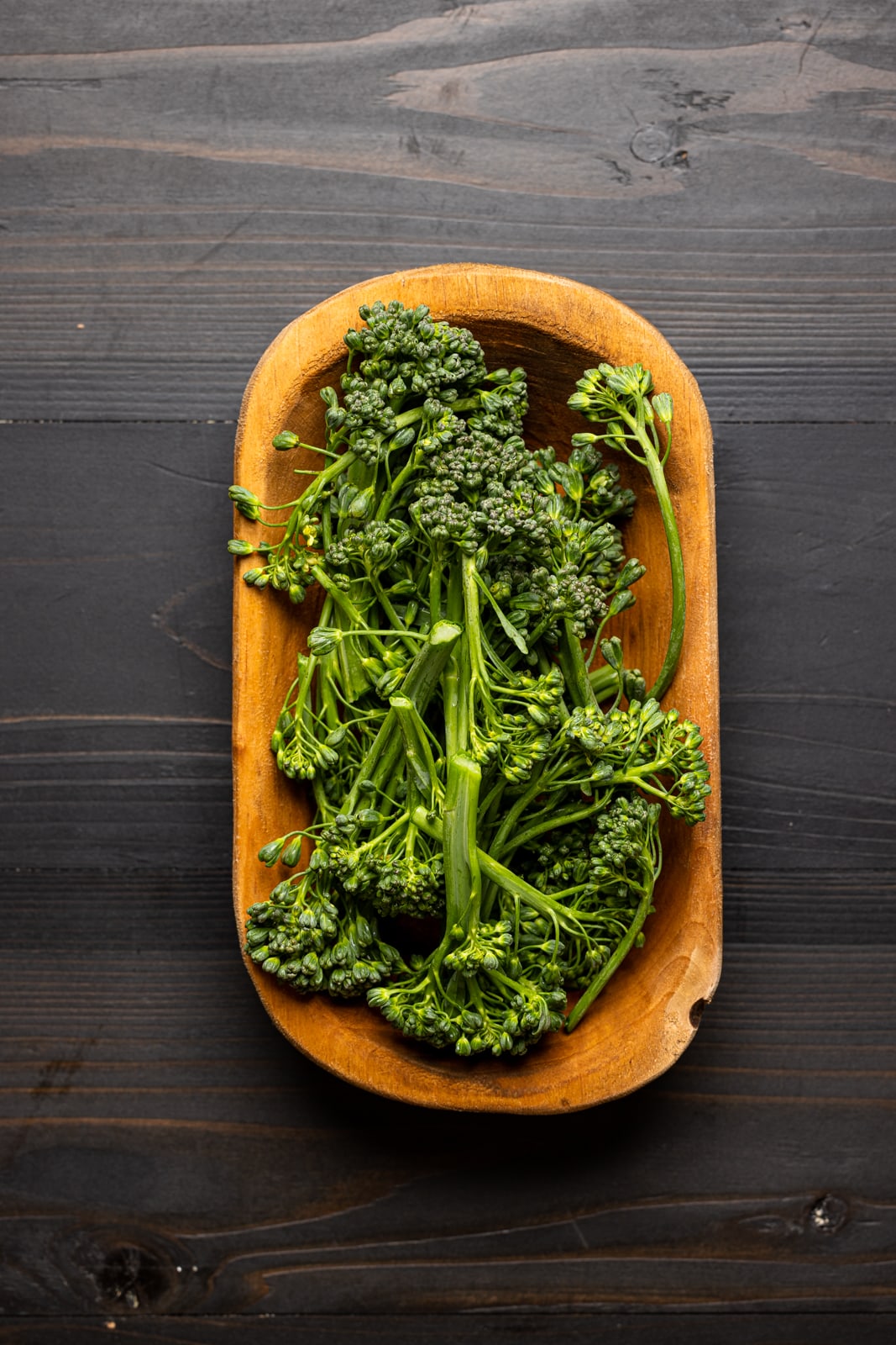 Broccolini in a wood bowl on a black table.