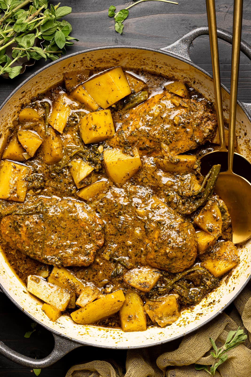 Pesto chicken and potatoes in a round dutch oven on a black table with two spoons.