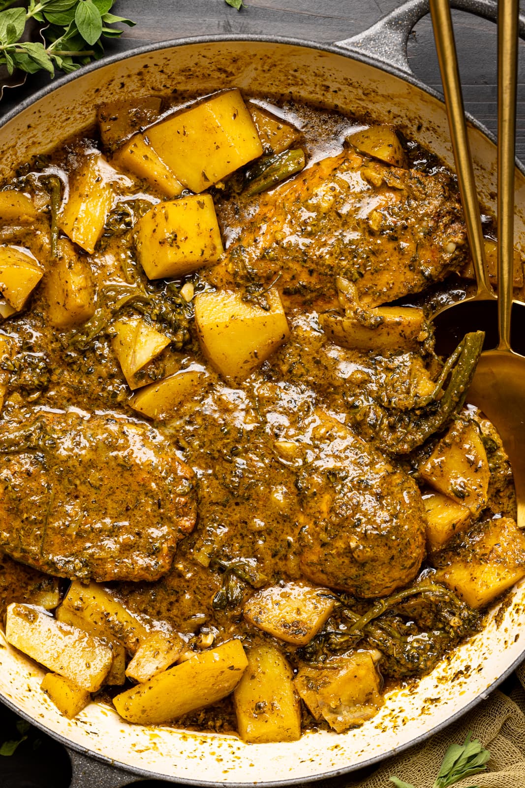 Up close shot of chicken and potatoes in a round dutch oven with two spoons.