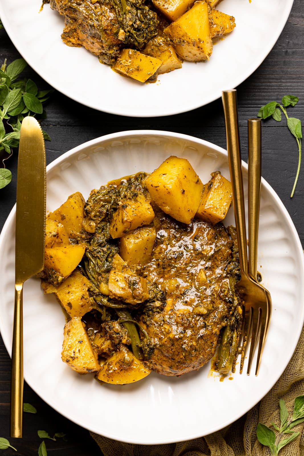 Chicken and potatoes in two white plates with forks and knives on a black table.