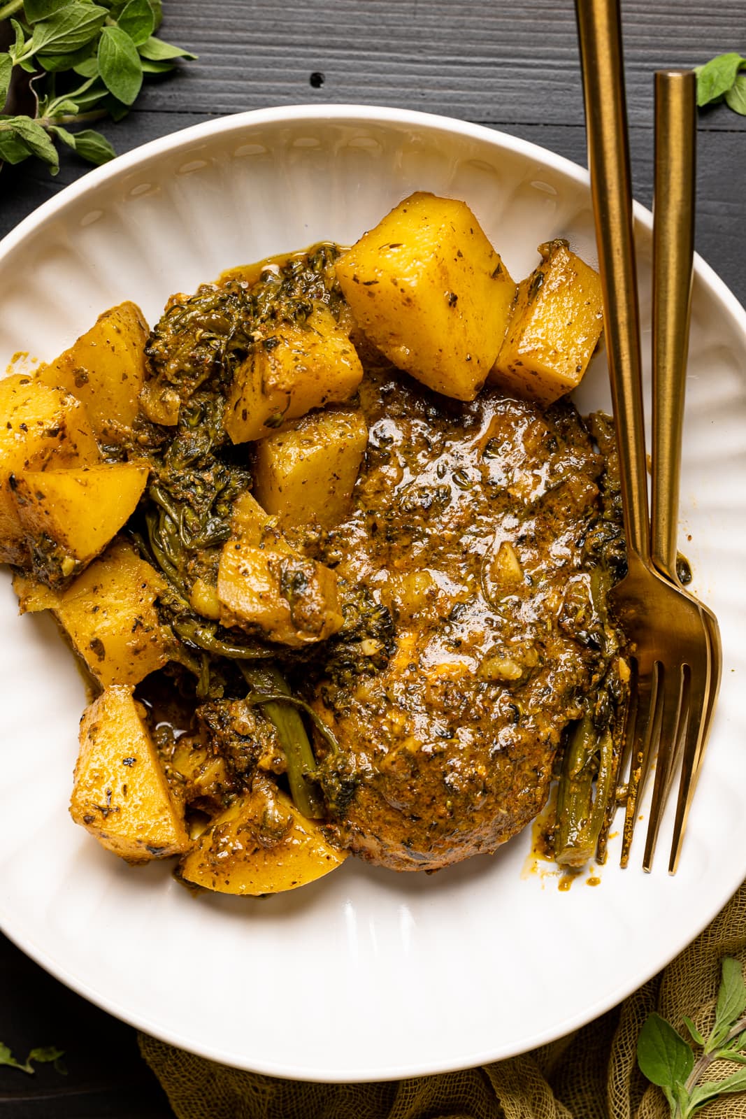 Pesto chicken and potatoes on a white plate/low bowl with two forks on a black table.