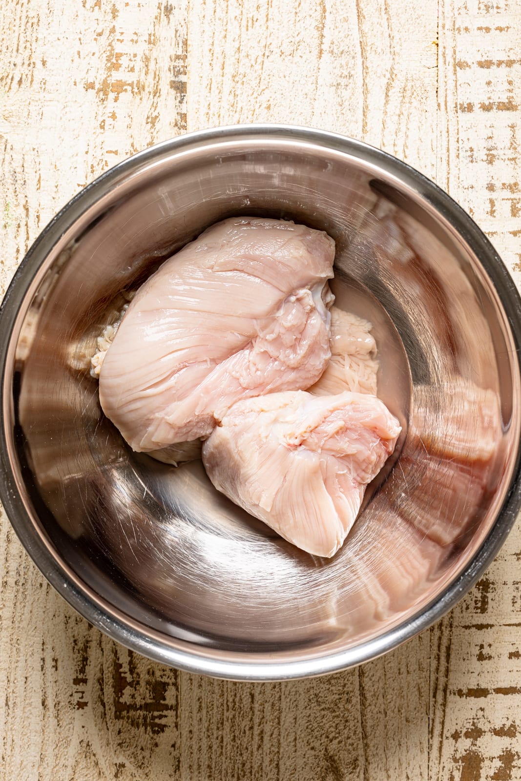 Clean raw chicken in a silver bowl on a white wood table.