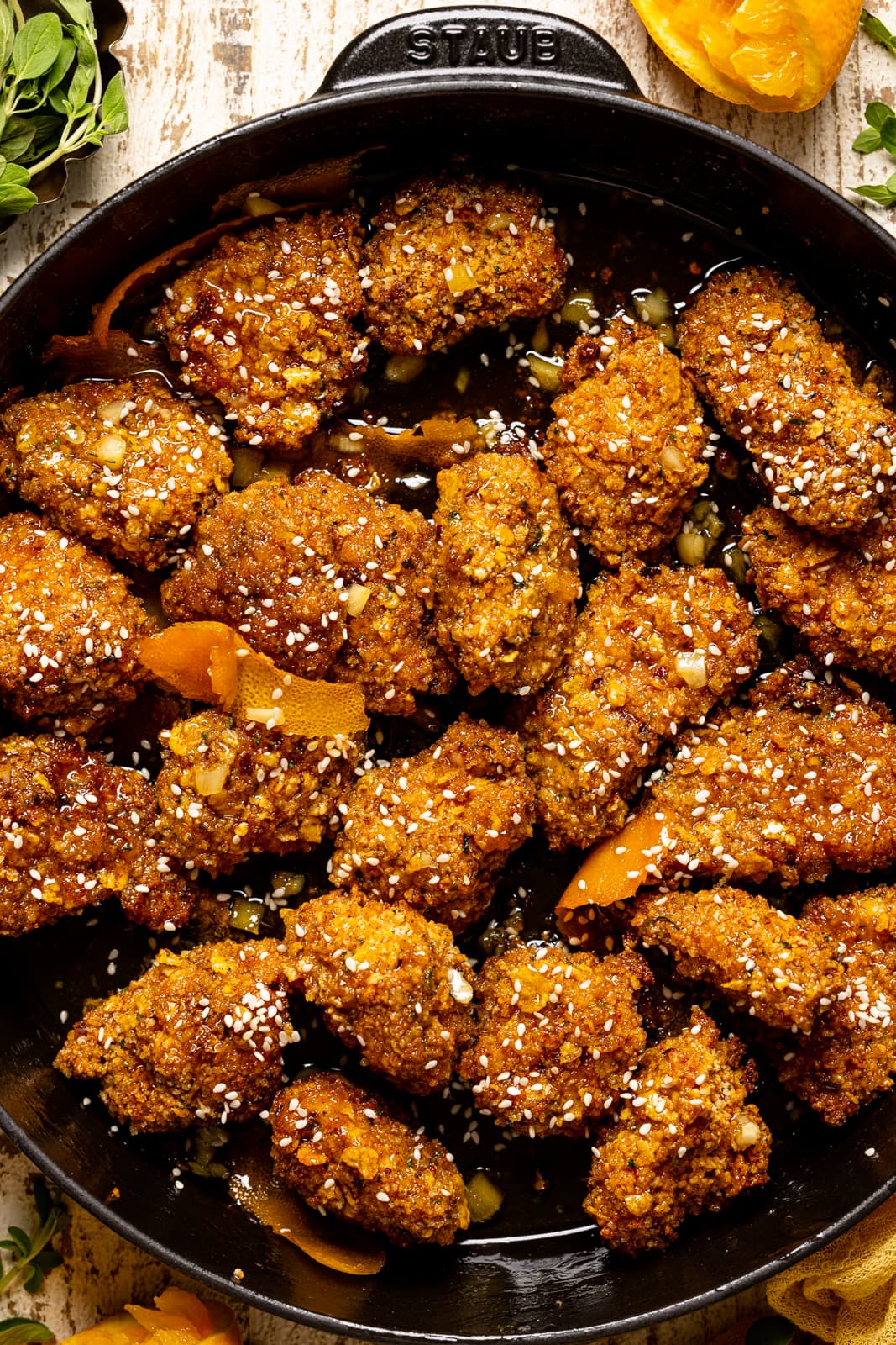 Up close shot of popcorn chicken in a black skillet with oranges and herbs.