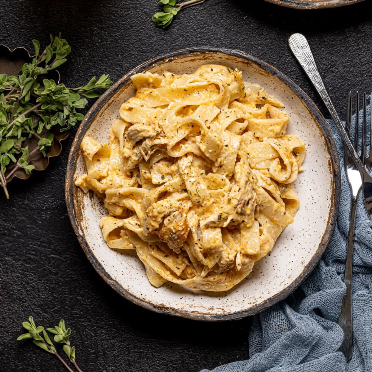 Alfredo on two white plates with two forks and a drink on a black table.