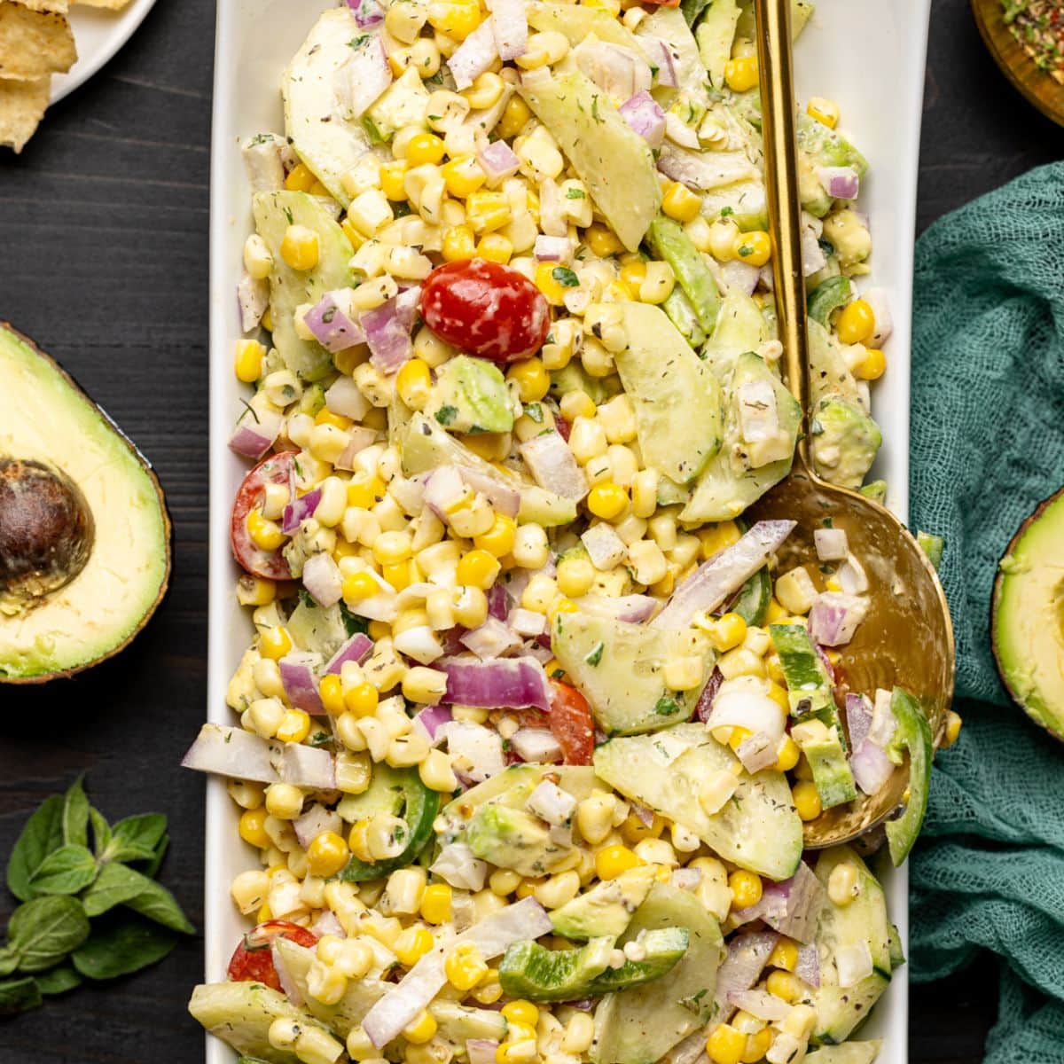 Salad in a long white plate with a spoon on a black wood table with tortilla chips and sliced avocados.