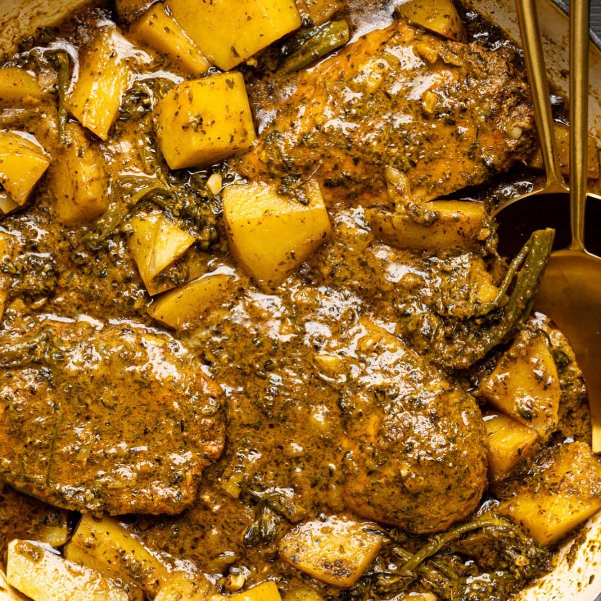 Up close shot of chicken and potatoes in a round dutch oven with two spoons.